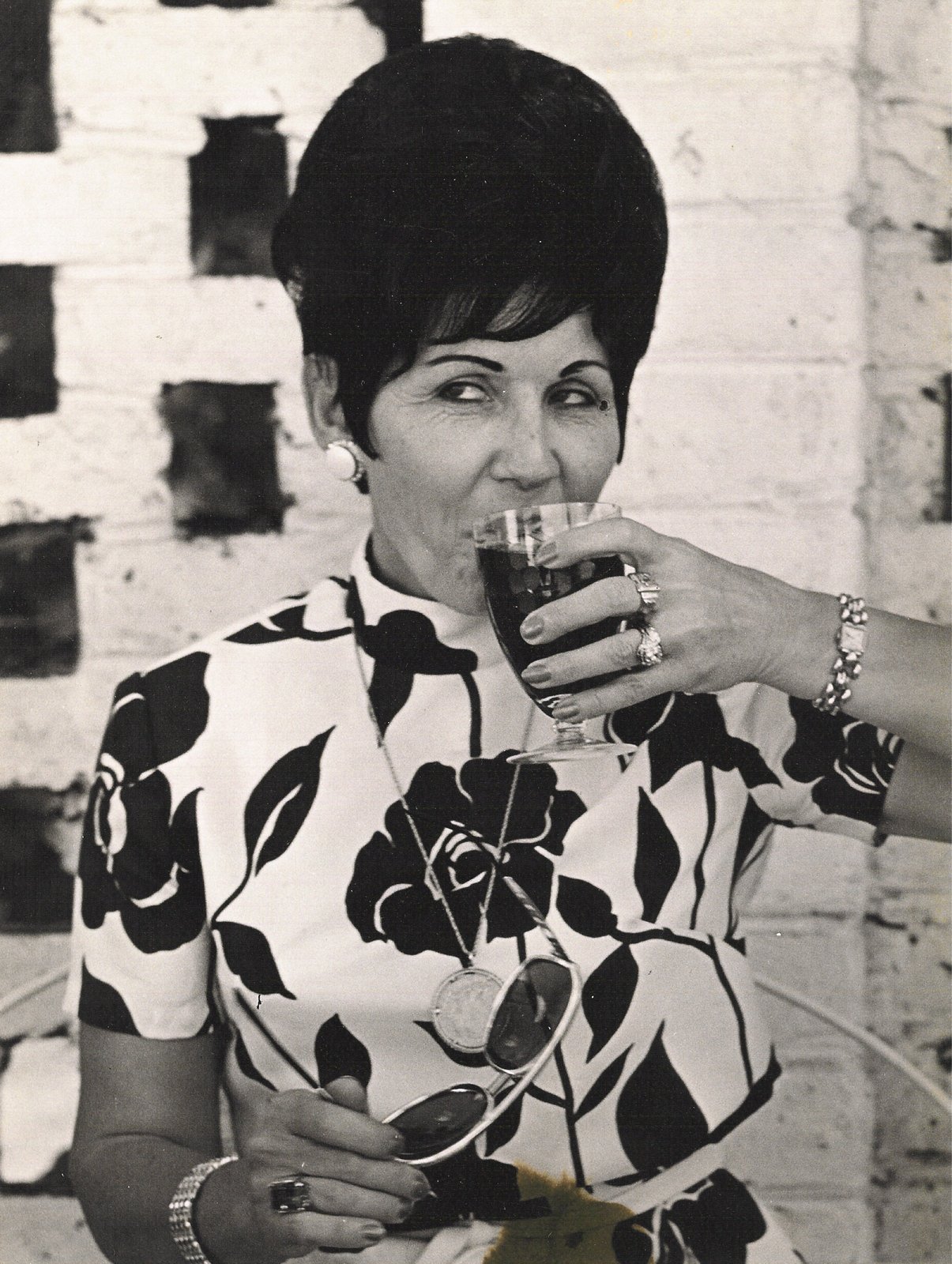 Portrait of a woman in a bold floral print raising a glass, late 1960s