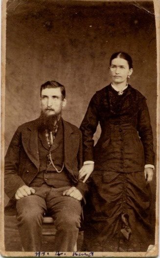 Carte-de-visite of a seated bearded man and a standing woman in a bustle dress.