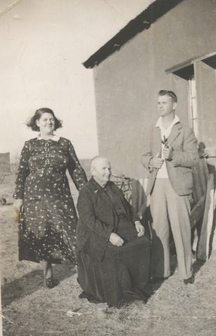 A young woman in a patterned dress, an elderly woman seated in black, and a young man outside a house.